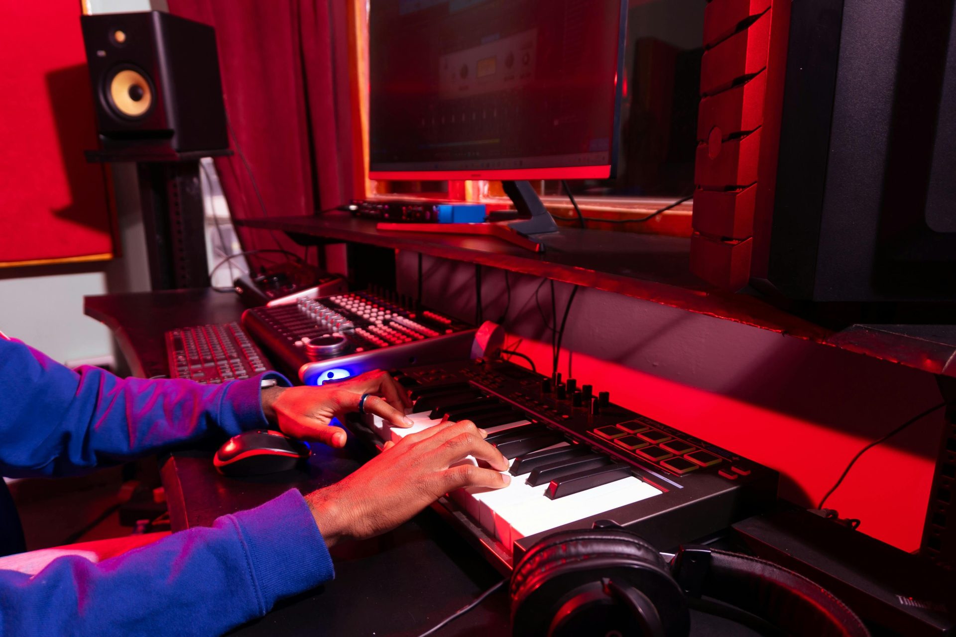 Eine Person, die in einem modernen Studio mit einem MIDI-Controller und einem Computer elektronische Musik erstellt.