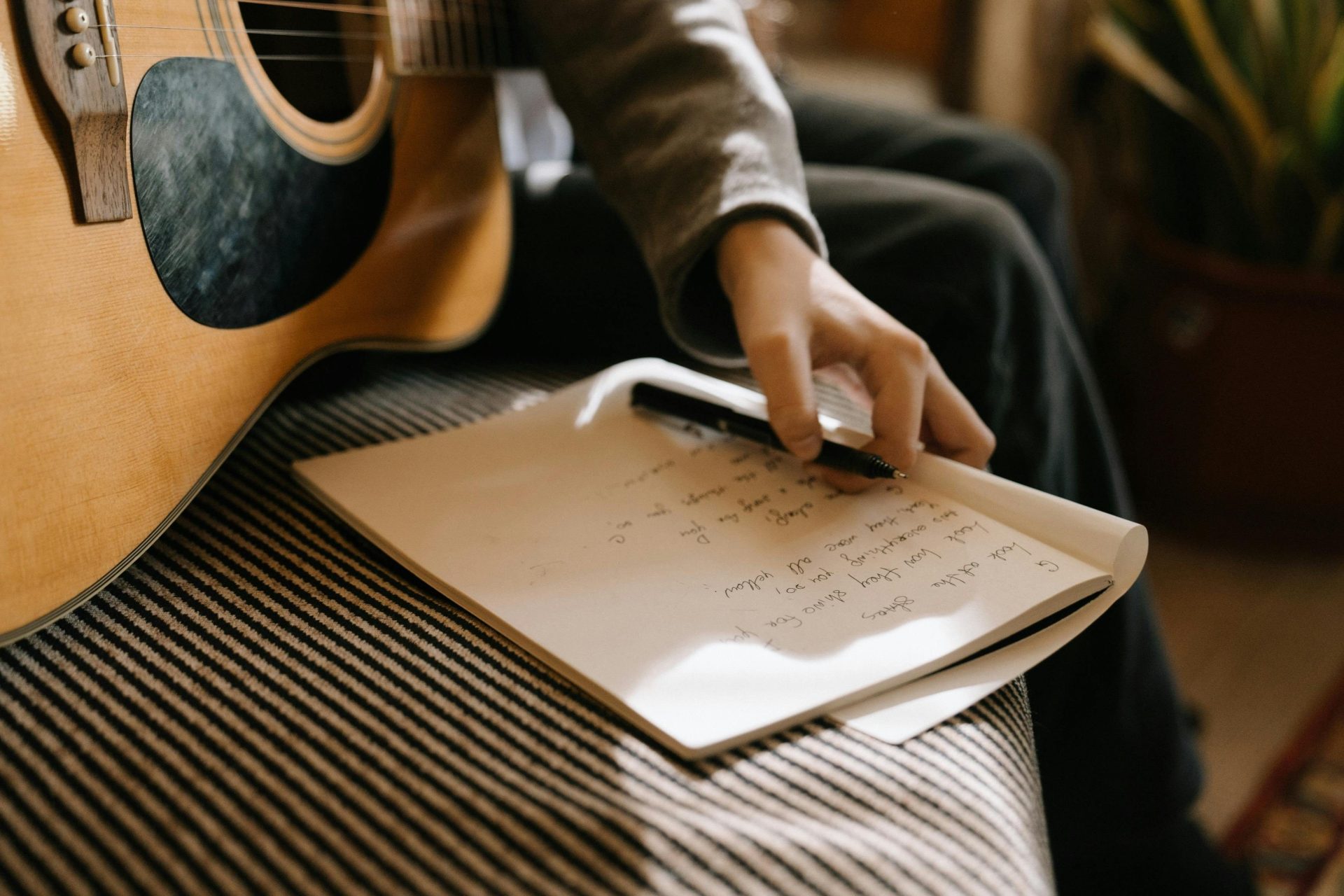 Eine Person, die Liedtexte mit einer Akustikgitarre schreibt und dabei Kreativität und musikalische Inspiration zum Ausdruck bringt.
