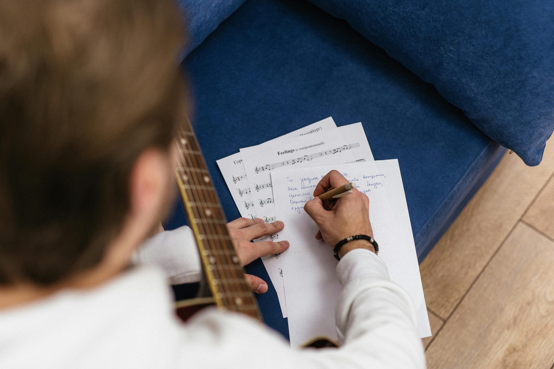 Ein Mann komponiert in einem Innenraum Musik auf einer Akustikgitarre mit handgeschriebenen Notizen.