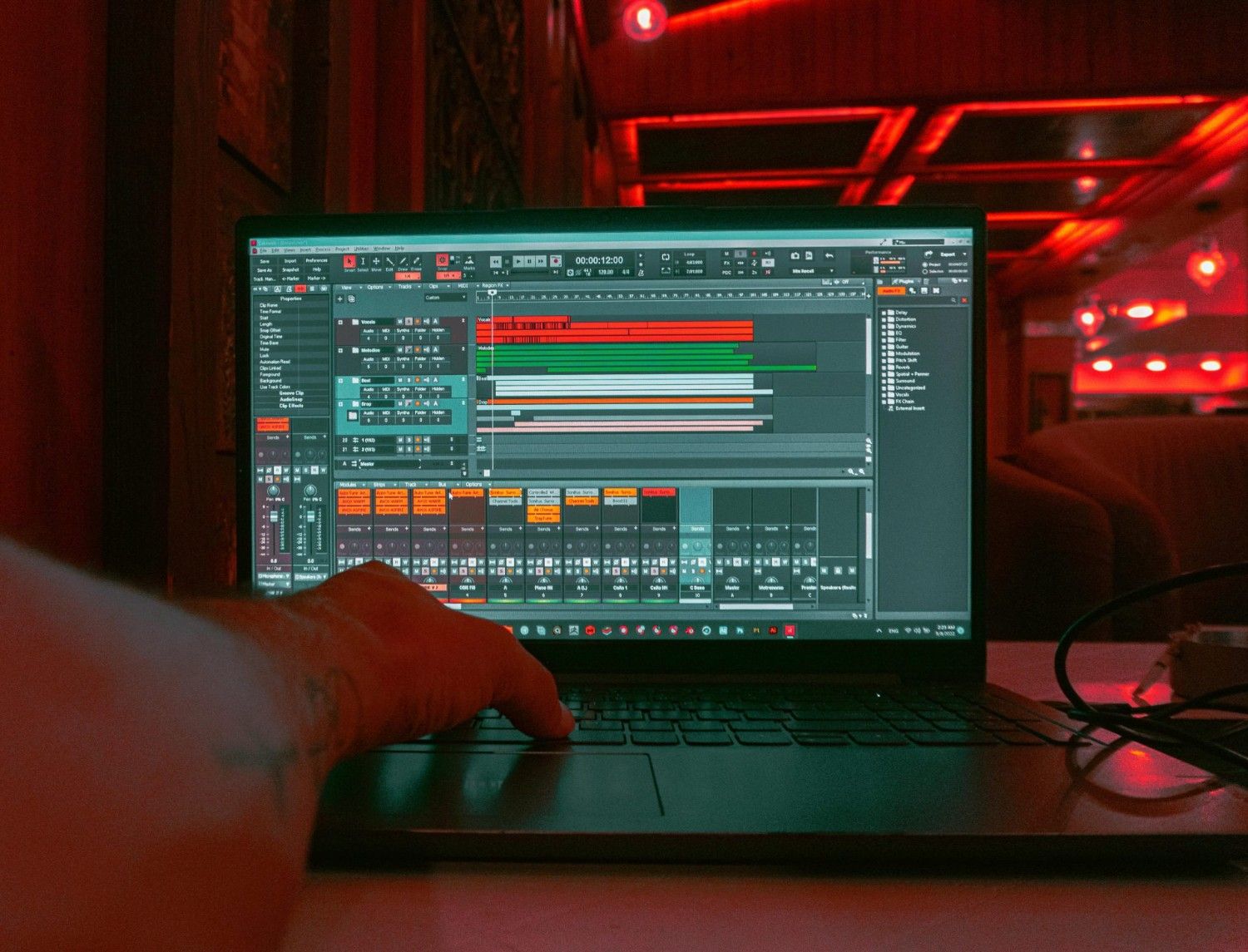 Eine Person bearbeitet Audiospuren an einem Laptop in einem Innenraum vor rotem Umgebungslicht.